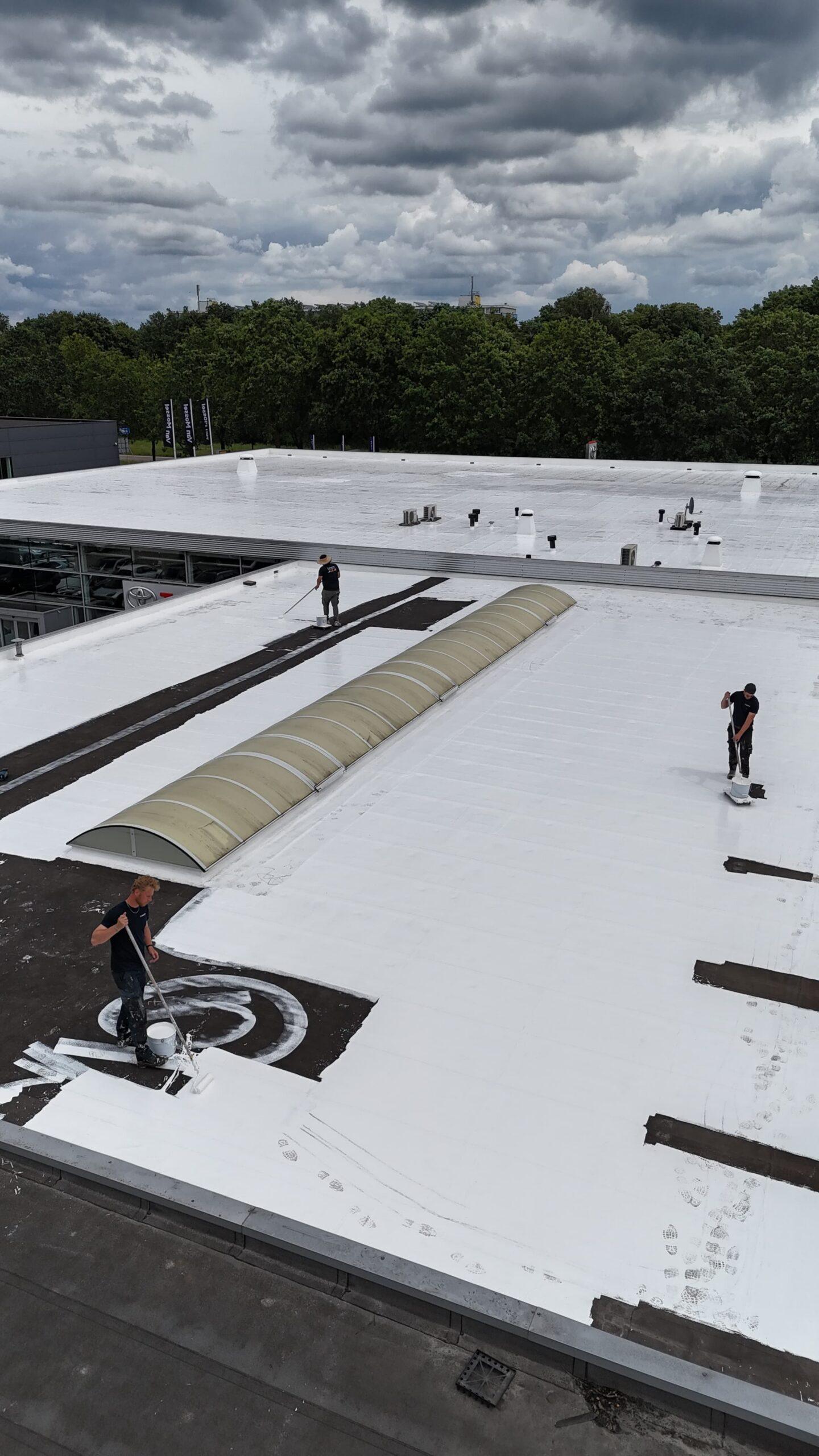 Dakwerkers van Recotex rollen de witte laag over een oud, donker plat dak
